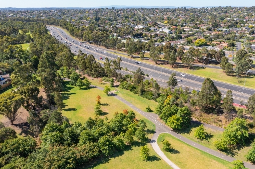 Horizontal aerial view of long, busy freeway with parkland on one side and suburbia on the other - Australian Stock Image