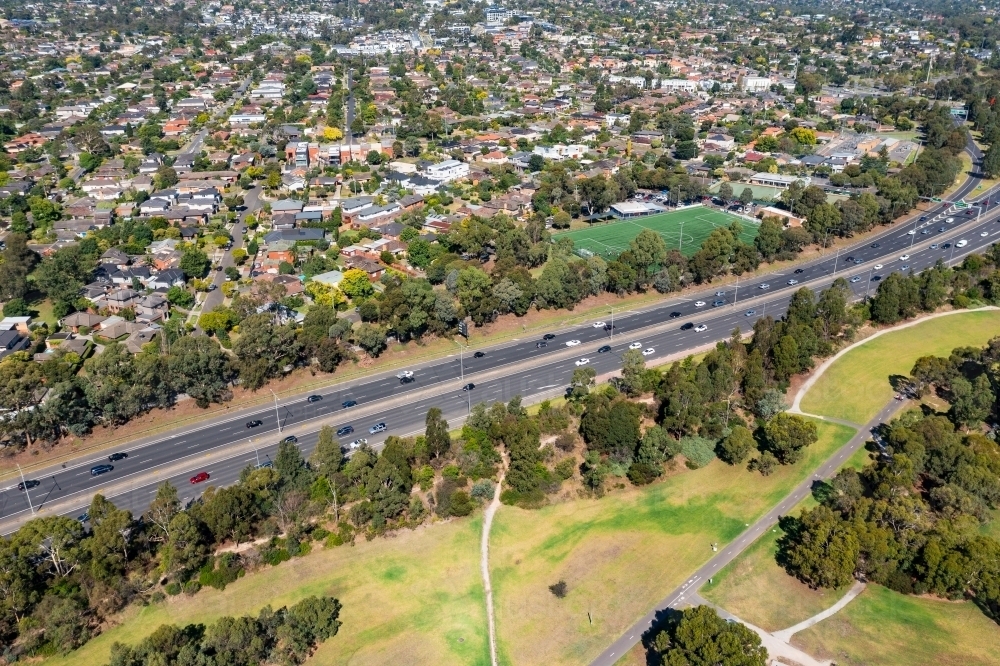 Aerial view of long, busy freeway with parkland on one side and suburbia on the other - Australian Stock Image