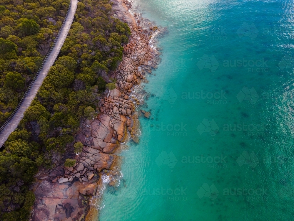 horizontal shot of ocean water with waves, bushes, trees, rocks and a long narrow road - Australian Stock Image