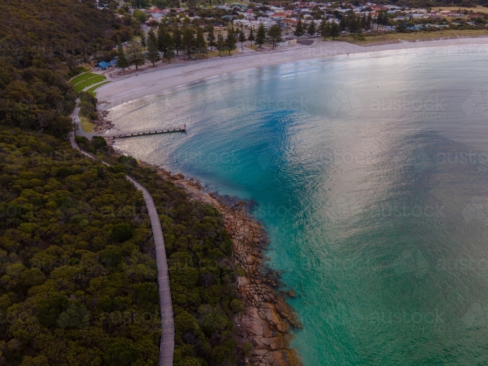 horizontal shot of ocean with sky reflection, bushes, trees, rocks, a narrow road and buildings - Australian Stock Image