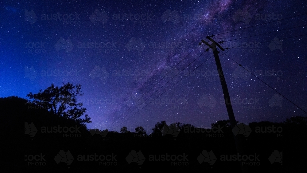 horizontal shot of some silhouette of trees, bushes and electric post of wires at dawn with stars - Australian Stock Image