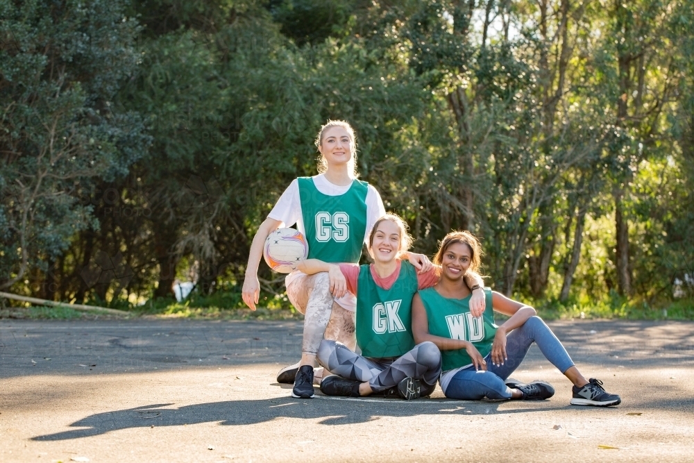 horizontal shot of three young smiling women sitting on the ground with one holding a net ball - Australian Stock Image