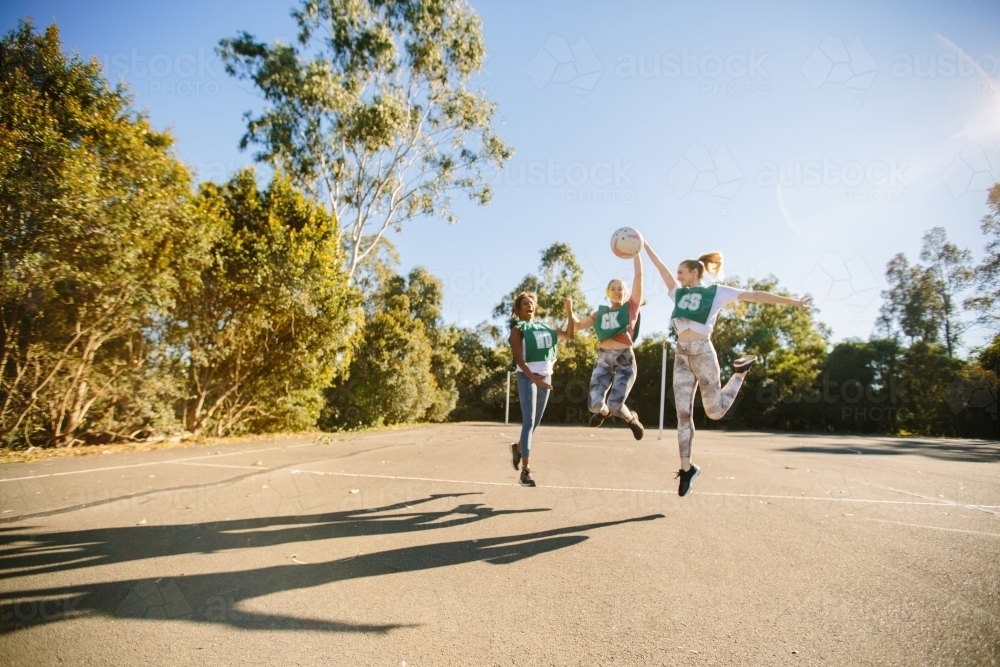 horizontal shot of three young women jumping in mid air on a sunny day with trees in the background - Australian Stock Image