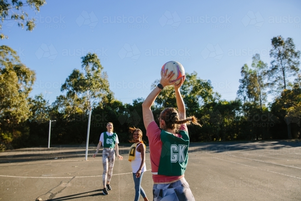 horizontal shot of three young women playing net ball in the field on a sunny day - Australian Stock Image