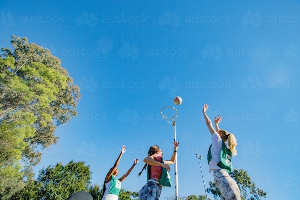 horizontal shot of three young women with arms raised up high playing net ball on a sunny day - Australian Stock Image