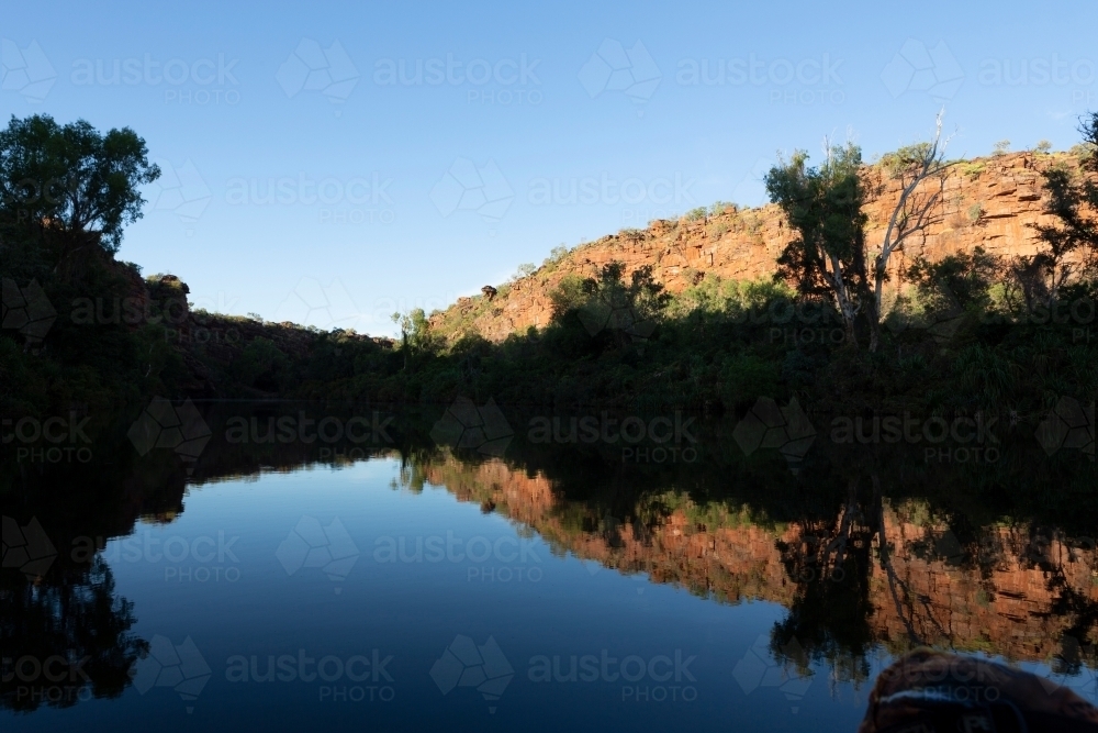 Horizontal shot of trees and mountains reflecting shadows in the water. - Australian Stock Image