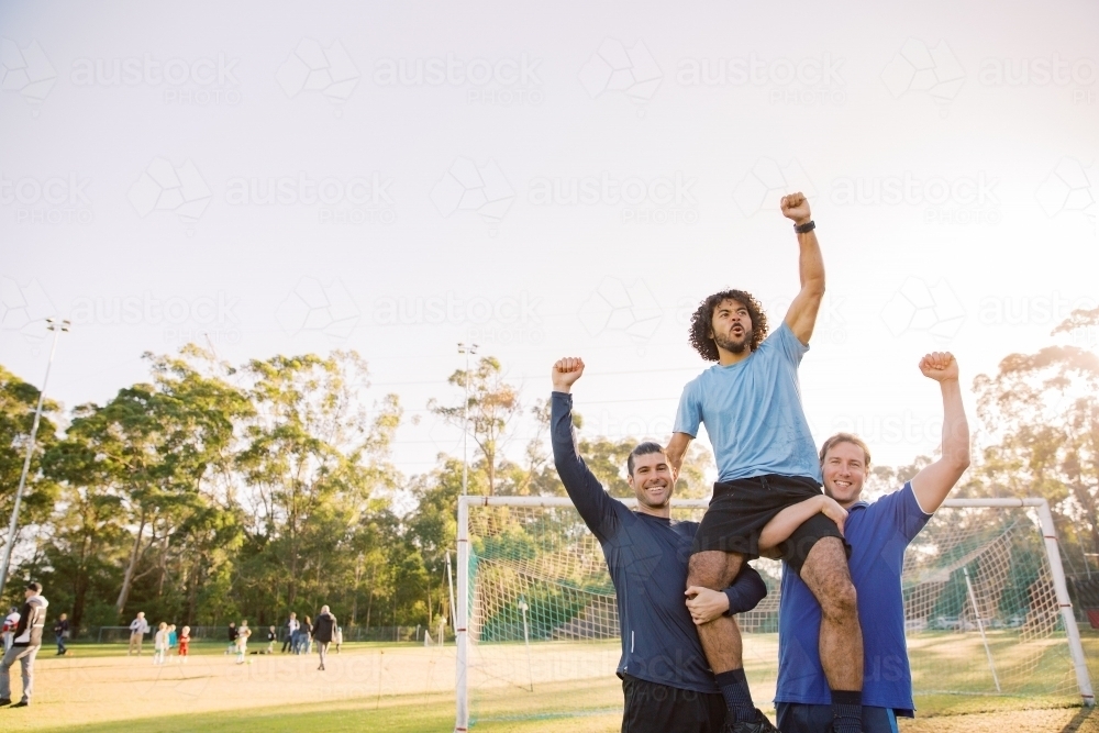 horizontal shot of two men carrying a man on their shoulders in a field on a sunny day - Australian Stock Image