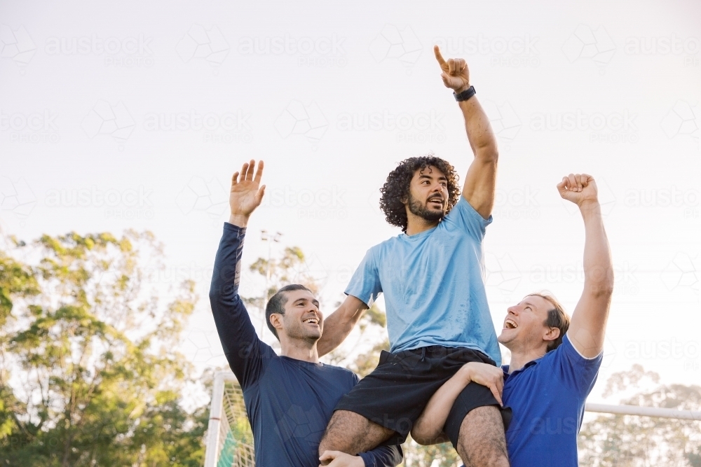 horizontal shot of two men carrying a man on their shoulders while raising their arms up high - Australian Stock Image