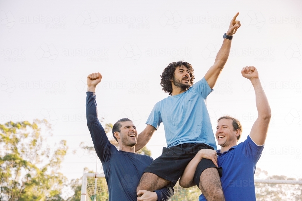 horizontal shot of two men carrying a man on their shoulders while raising their arms up high - Australian Stock Image