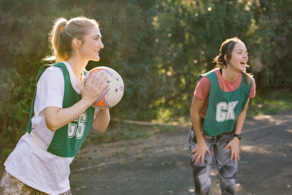 horizontal shot of two young women playing net ball in a sunny day with trees in the background - Australian Stock Image