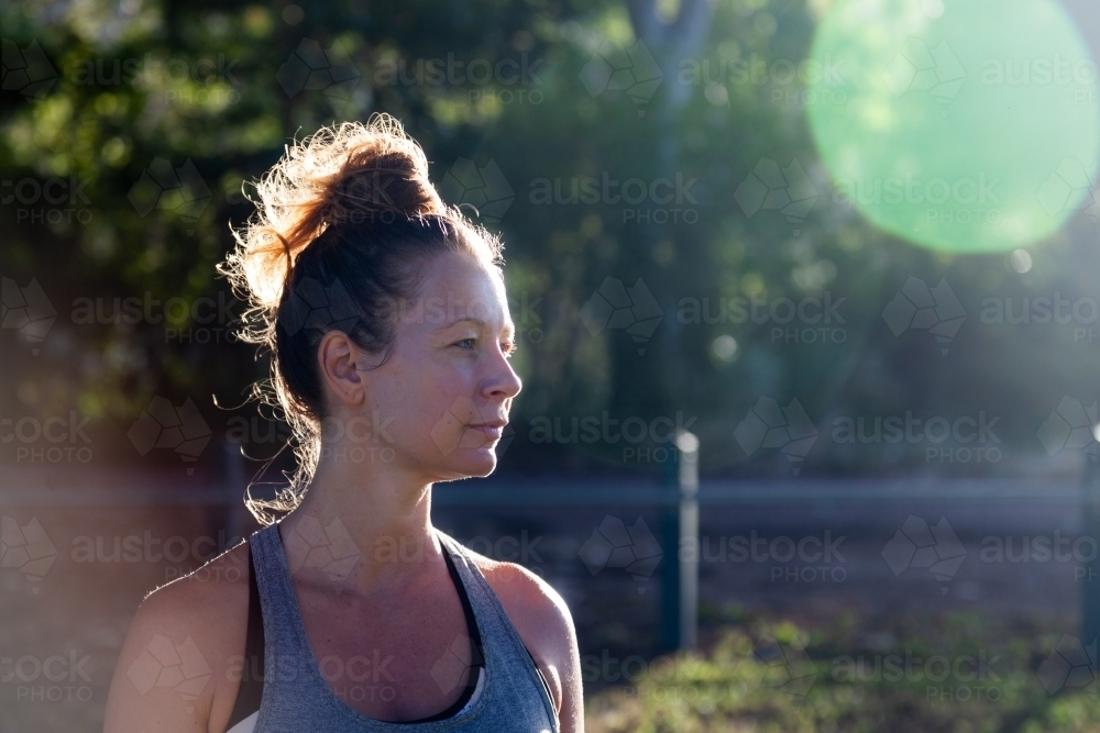 horizontal shot of woman with messy bun hairstyle looking from a far with sunlight and trees - Australian Stock Image