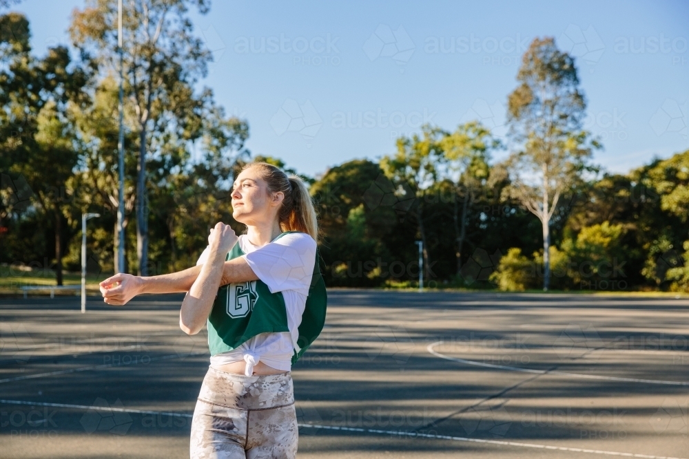 horizontal shot of young woman stretching on a sunny day with trees in the background and clear sky - Australian Stock Image