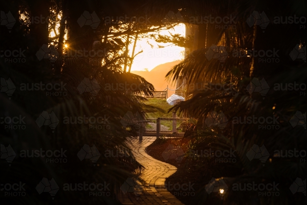 horizontal silhouette shot of a sunset with tiled walkway leaves and wooden chair outside - Australian Stock Image