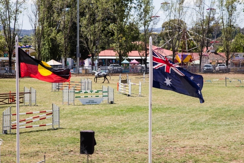 Horse jumping event between Aboriginal and Australian flags at local show - Australian Stock Image