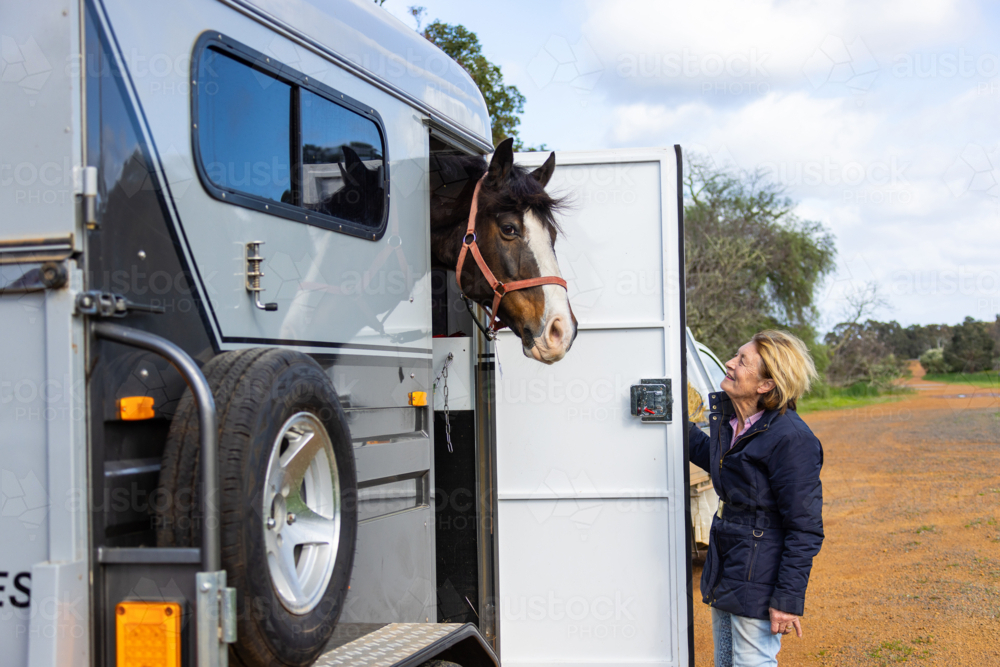 Horse loaded in a trailer with senior woman standing outside. - Australian Stock Image