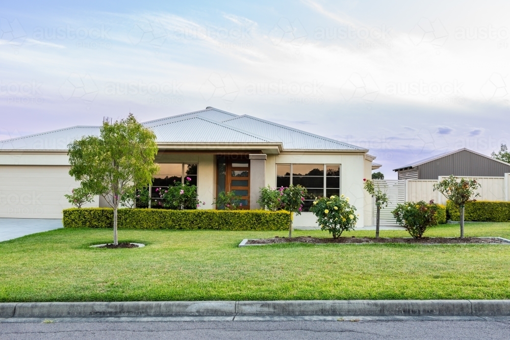 House with neat front garden and lawn at dusk in suburban area - Australian Stock Image