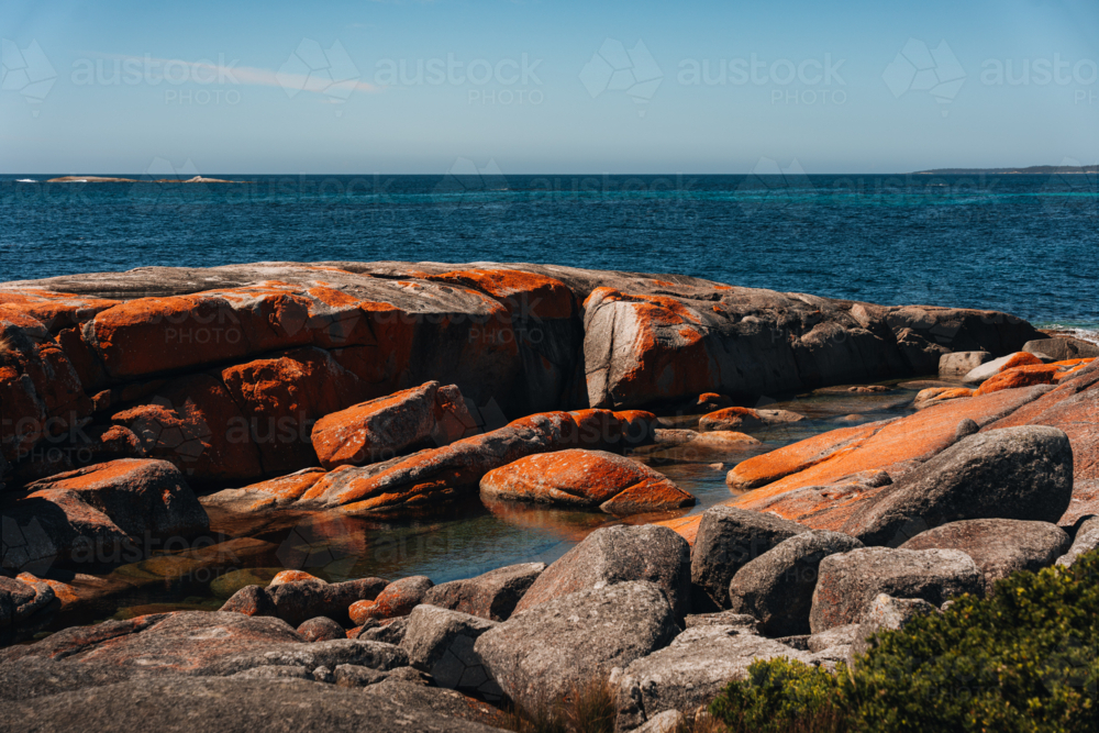 Huge reddish rocks along the shoreline with blue waters - Australian Stock Image