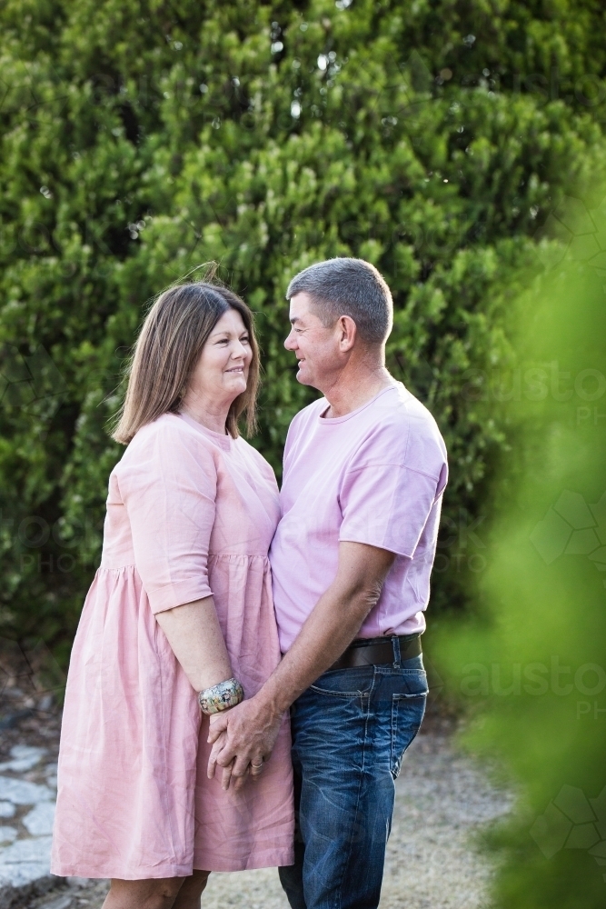 Husband and wife couple standing holding hands smiling at each other - Australian Stock Image