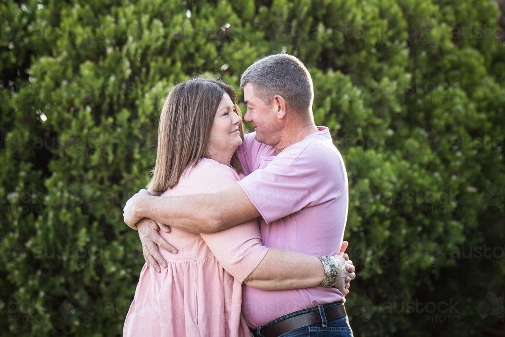 Husband and wife standing arm in arm hugging looking at each other - Australian Stock Image