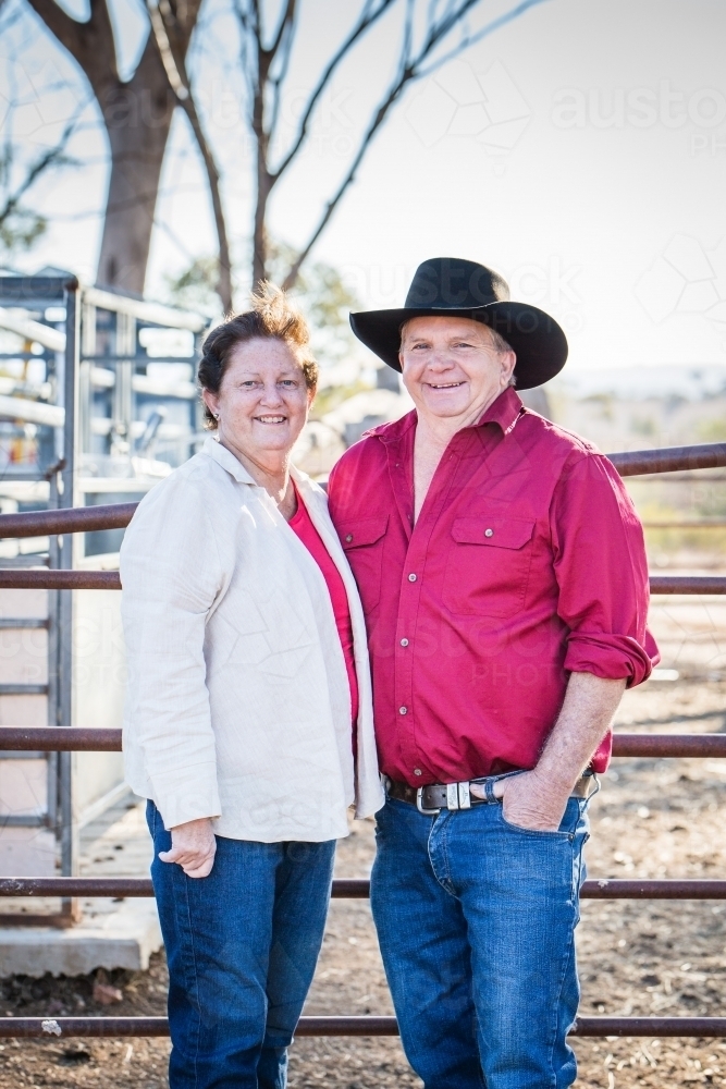 Husband and wife standing together smiling on farm in drought - Australian Stock Image