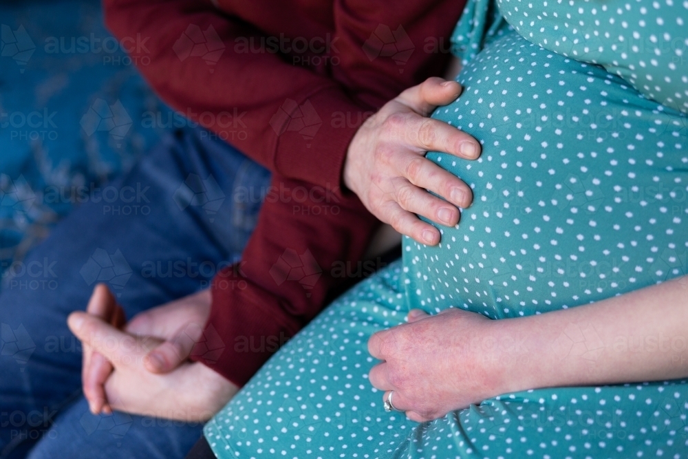 husband putting hand on pregnant wife's belly praying together - Australian Stock Image