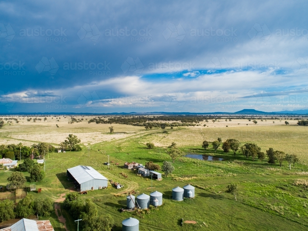 Incoming rain storm over farm with outbuildings and dam in green paddock - Australian Stock Image