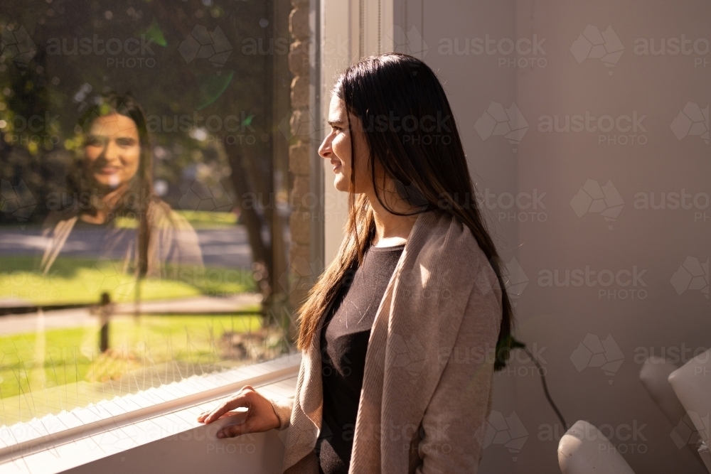 Indian woman standing by the window looking outside on a sunny day - Australian Stock Image