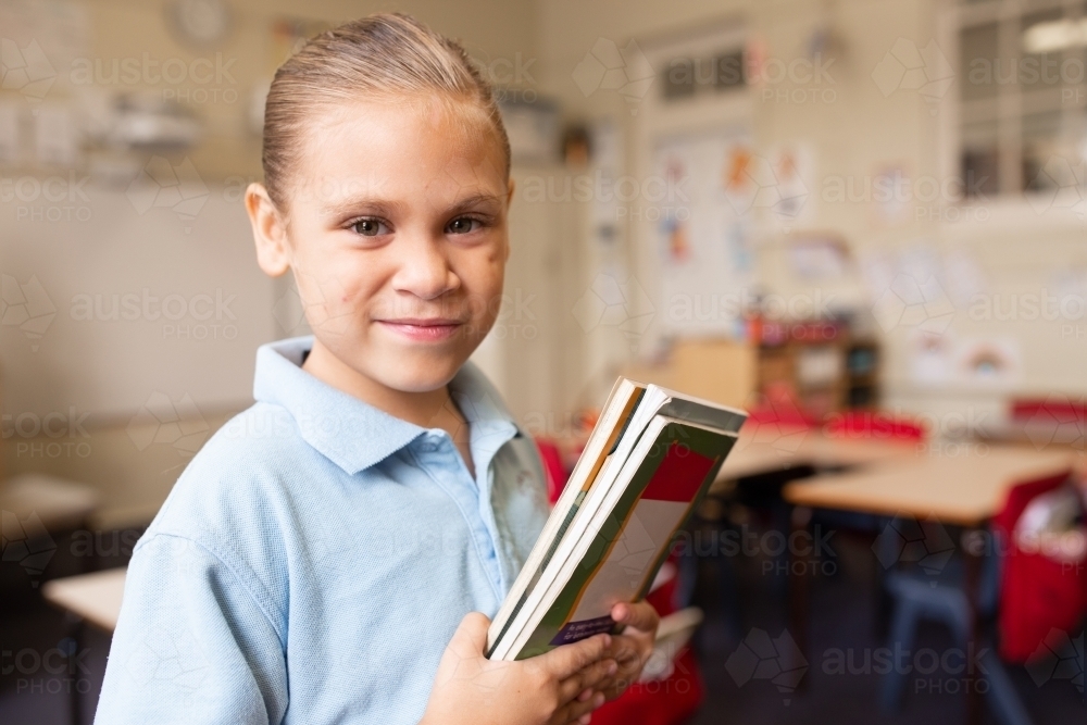 Indigenous girl primary school student with a book in a classroom - Australian Stock Image