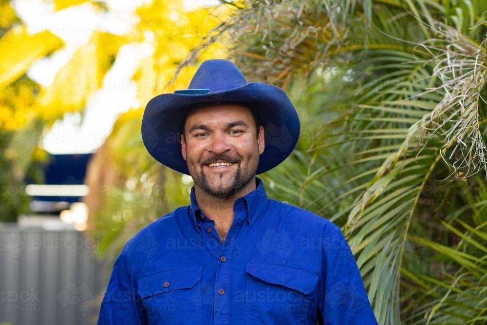 indigenous man in his late twenties dressed in blue shirt and blue hat smiling - Australian Stock Image