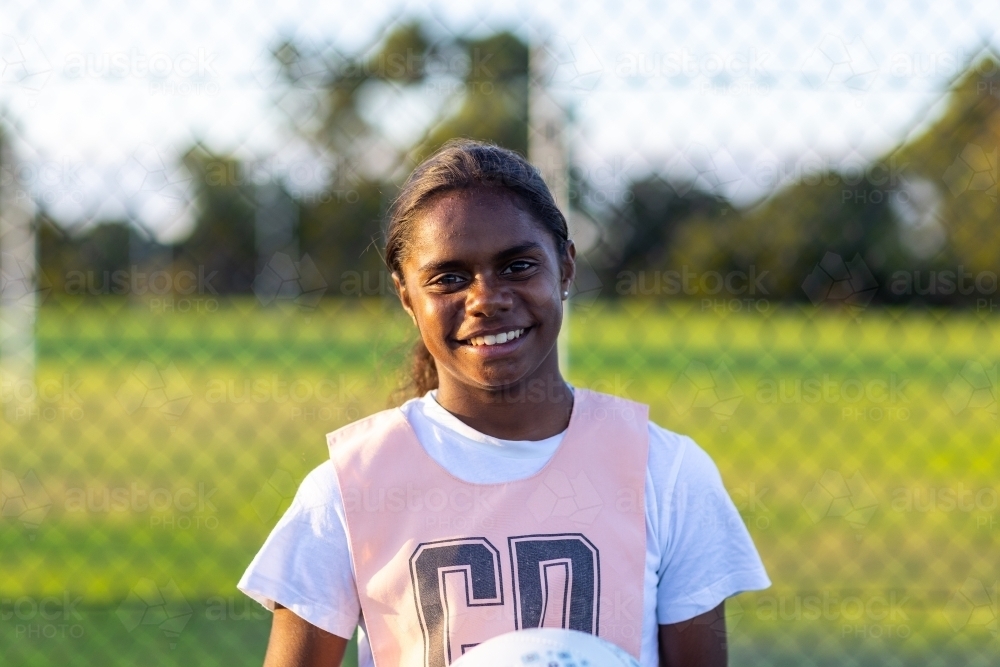 indigenous netball player in front of fence looking at camera - Australian Stock Image