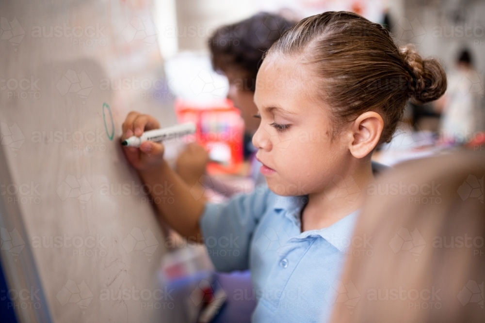 Indigenous primary school girl student drawing on a whiteboard - Australian Stock Image