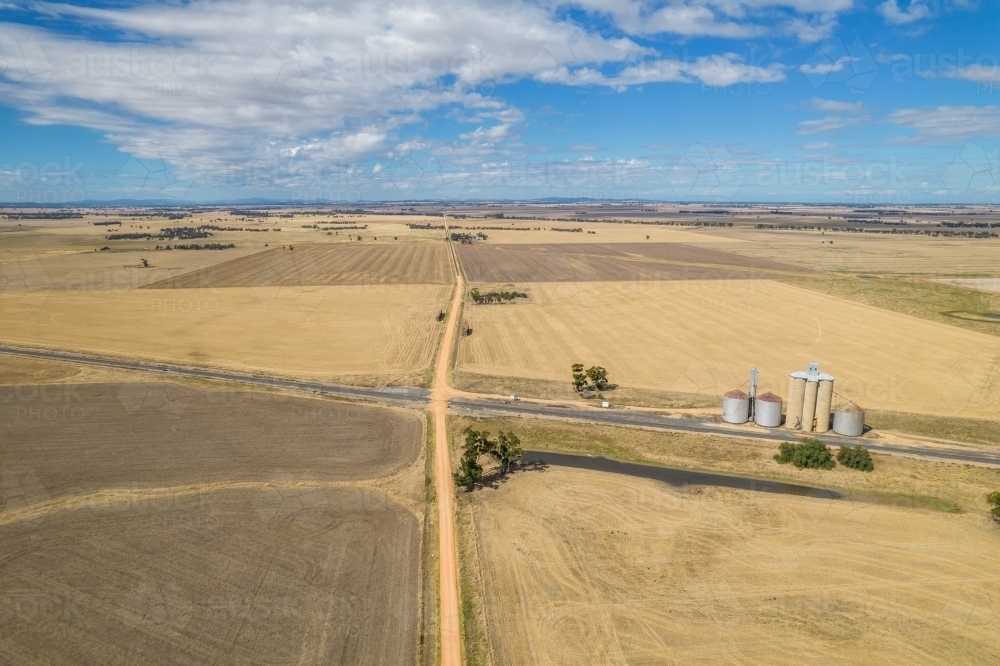 Intersection of dirt and asphalt road with the silos seen to the right. - Australian Stock Image