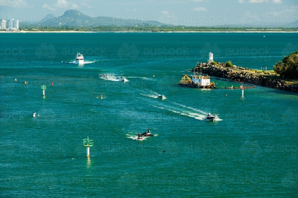 Jet skis and a boat entering a river mount with mountains in background and navigation markers - Australian Stock Image