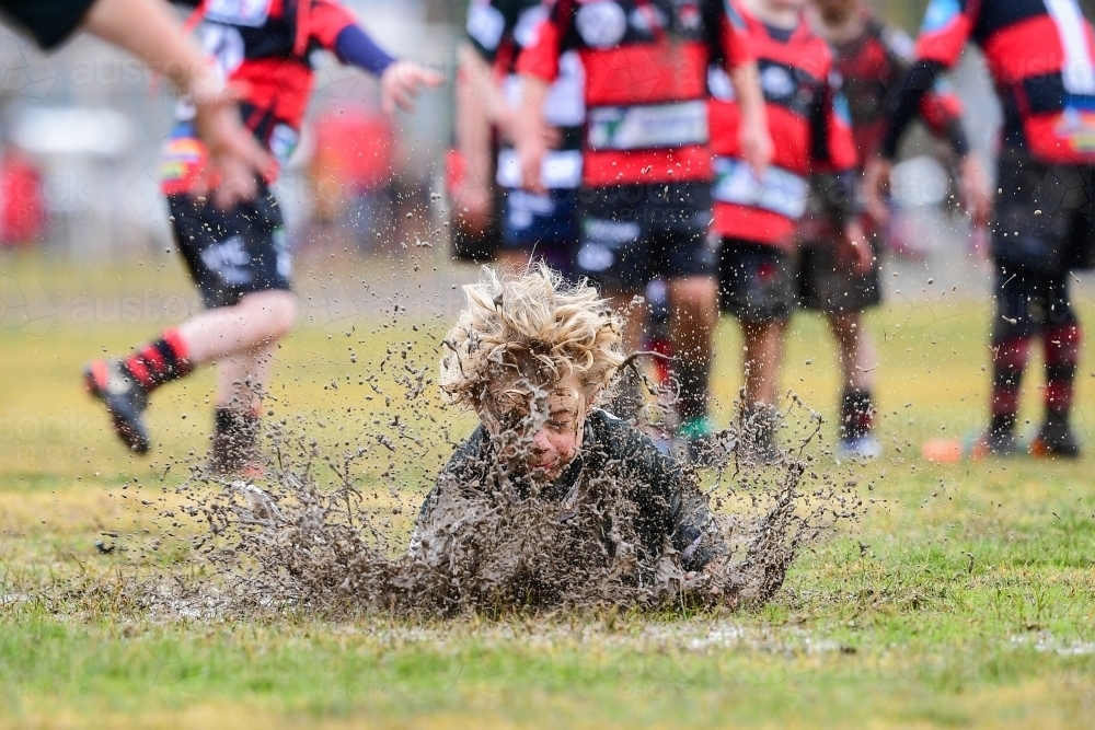 Junior rugby player belly slides in the mud - Australian Stock Image