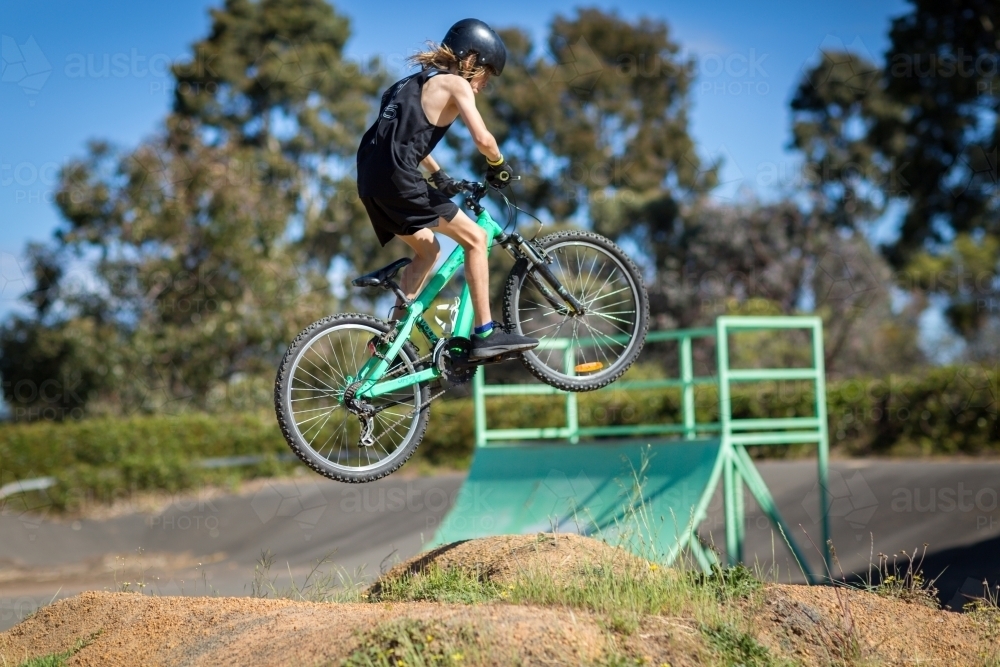 Kid getting air jumping bike over mound - Australian Stock Image