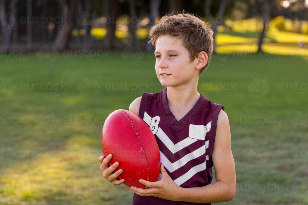 kid holding a football outside and looking away - Australian Stock Image