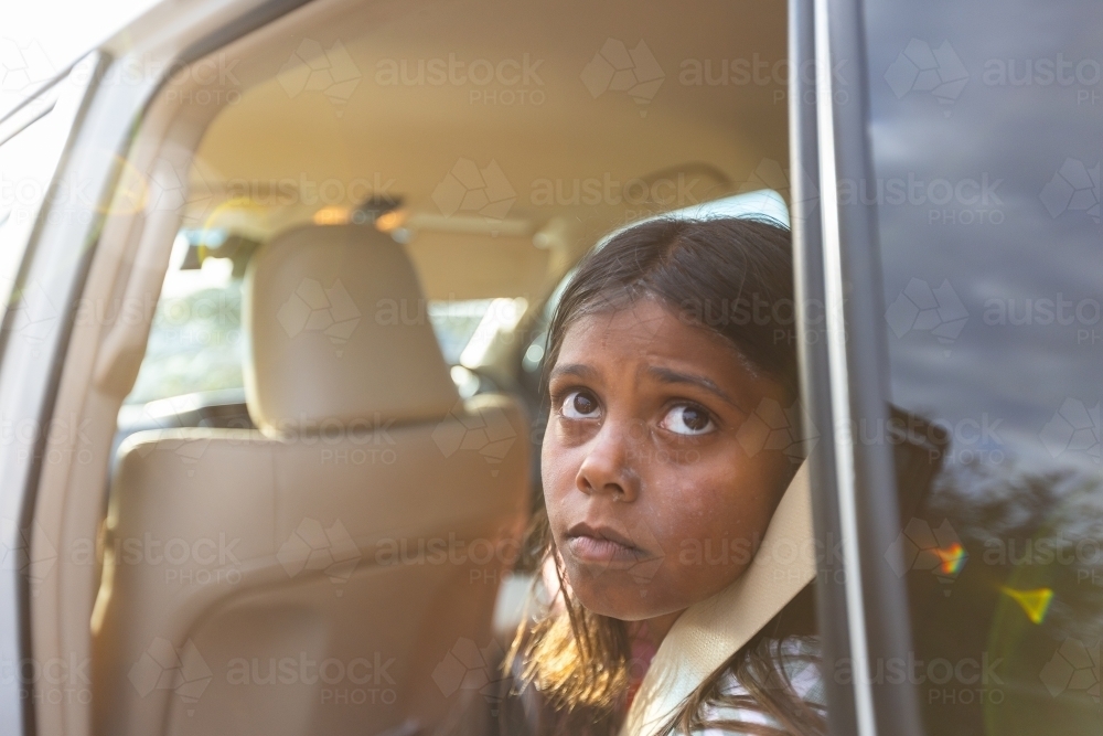 kid in back seat looking out open door of car - Australian Stock Image