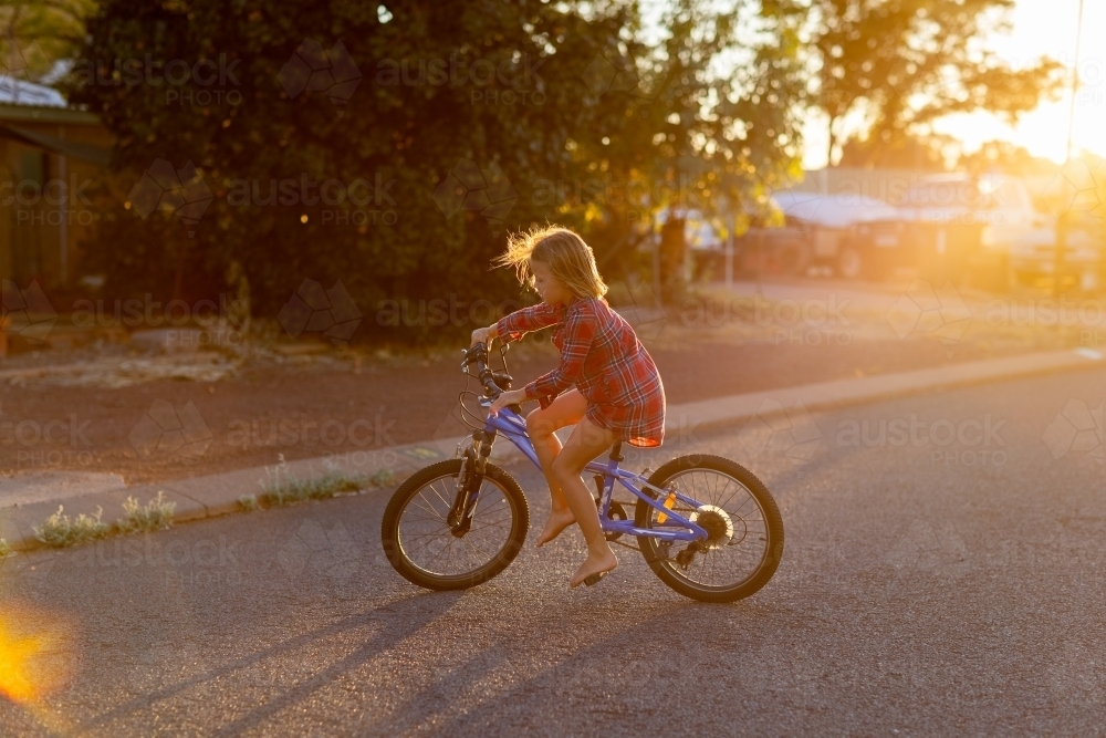 kid riding her bike on quiet street in golden light - Australian Stock Image