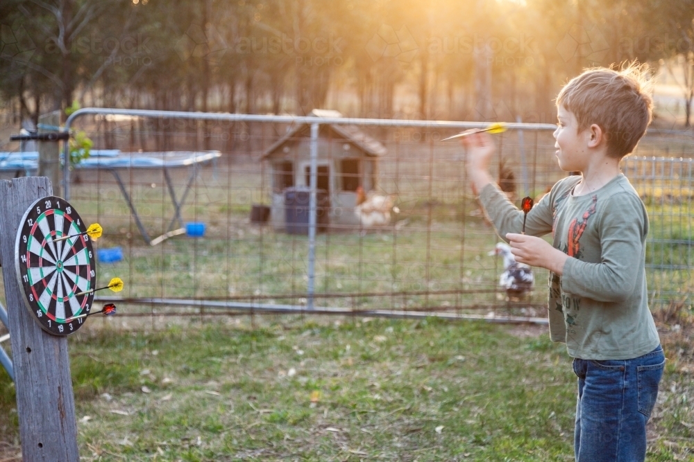 Kid throwing darts at dart board outside - Australian Stock Image