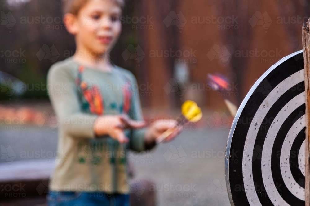 Kid throwing darts at dart board outside - Australian Stock Image