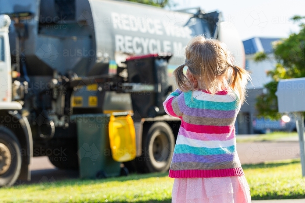 Kid watching noisy garbage truck emptying bin with hands over ears - Australian Stock Image