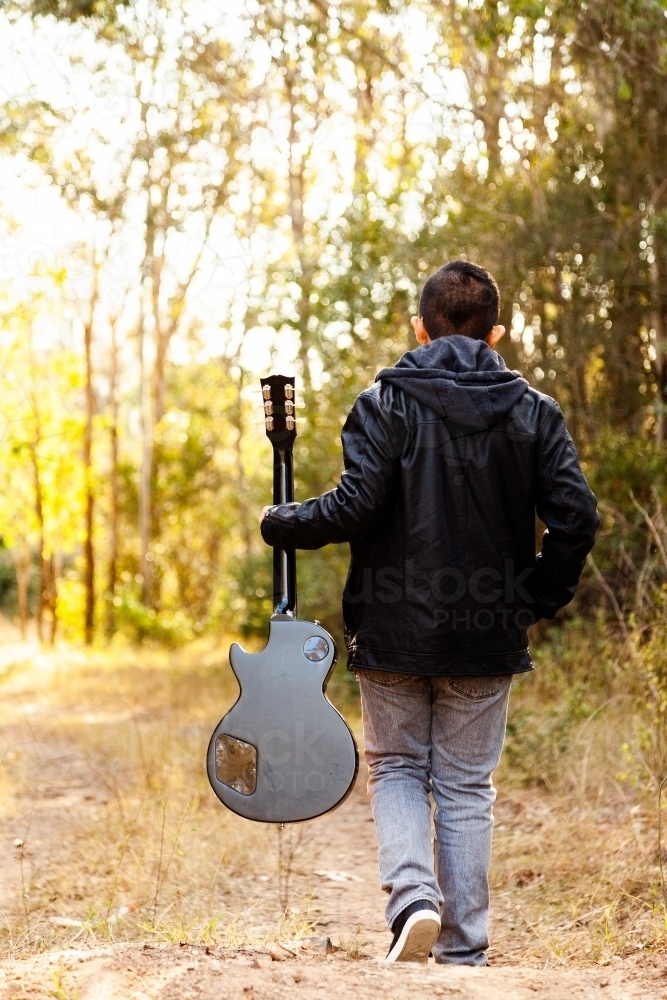 Kid with guitar walking away down path in bushland - Australian Stock Image