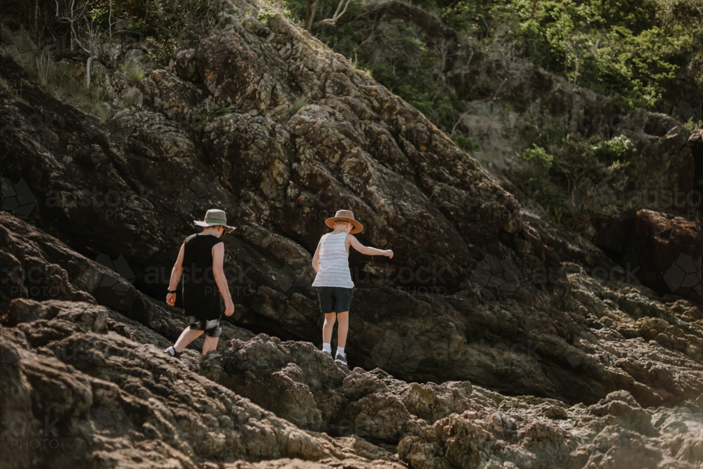 Kids adventuring across coastal rocks at Coral Beach near Shute Harbour in The Whitsundays - Australian Stock Image