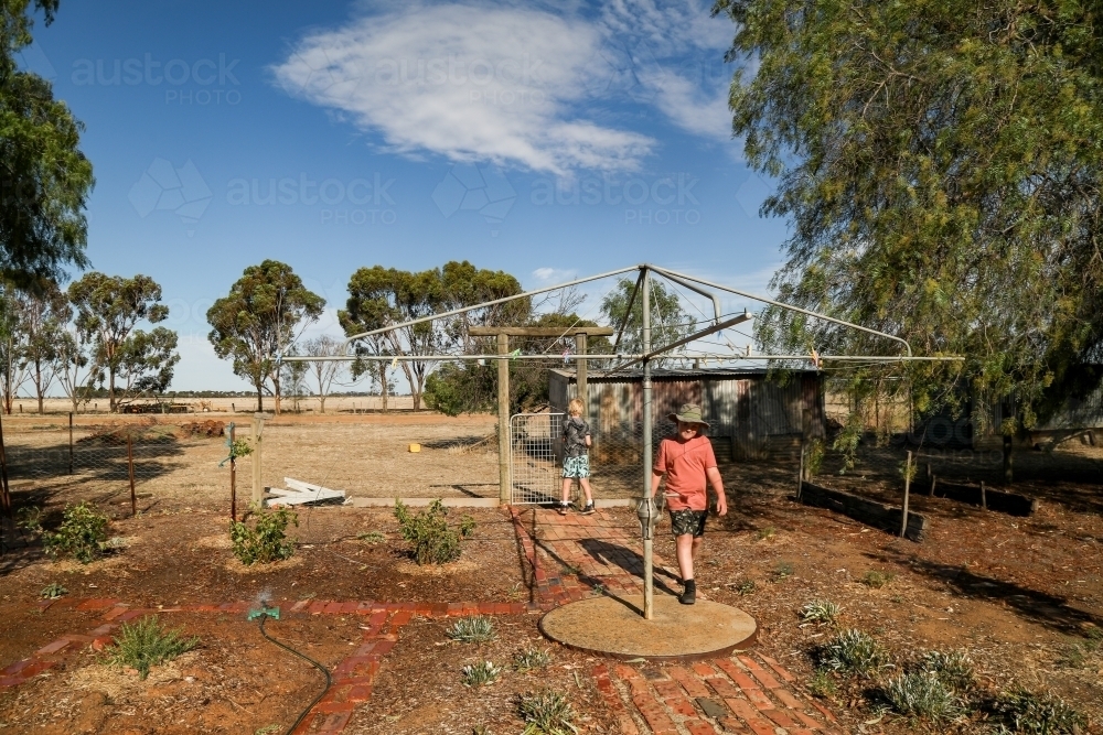 Kids in rural dry backyard in summertime with hills hoist washing line - Australian Stock Image