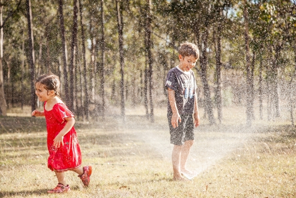 Kids playing under a sprinkler in summer - Australian Stock Image