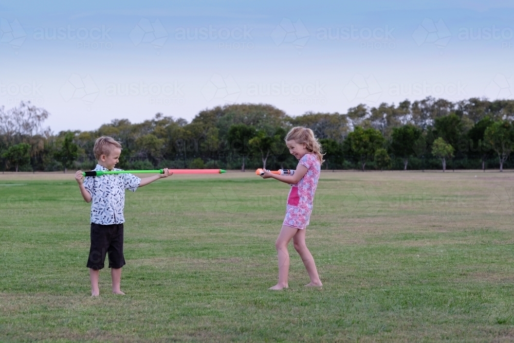 Kids playing with water guns in the park - Australian Stock Image