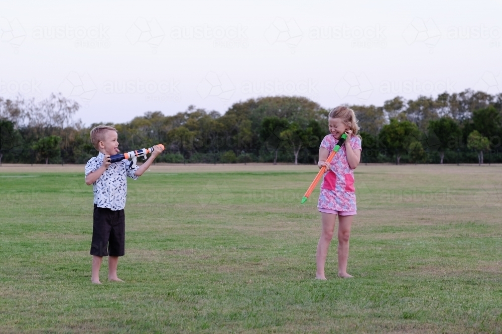 Kids playing with water guns in the park - Australian Stock Image