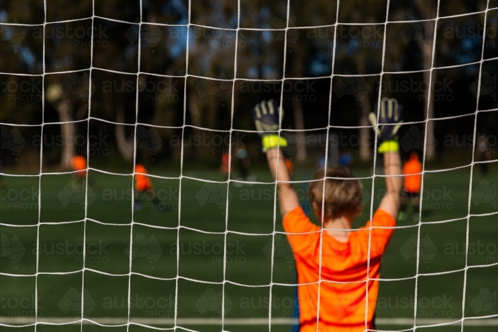 kids soccer game on a sunny day with a goalie with gloves in the air - Australian Stock Image