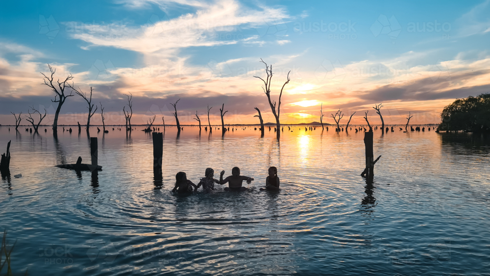 Kids swimming at Kow Swamp in rural Victoria at sunset - Australian Stock Image