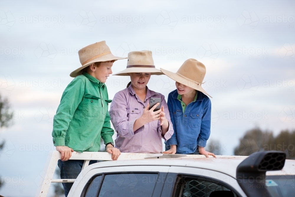 Kids use a phone to take photos on the back of a ute - Australian Stock Image